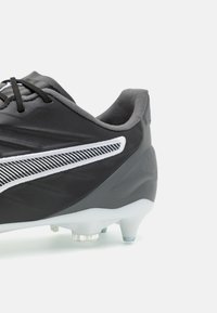 Scarpini da calcio neri con upper sintetico testurizzato, strisce bianche a contrasto e tacchetti trasparenti stampati per la trazione su superfici erbose.