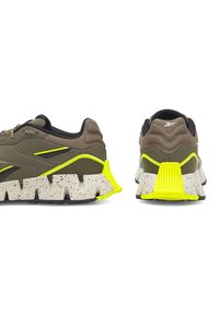 Brązowe trampki z teksturowanym wzorem, z neonowo żółtym akcentem i białą, nakrapianą podeszwą. Amortyzowana pięta i gładkie, czarne wnętrze.