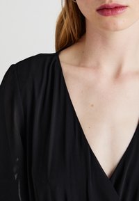 Black, v-neck dress with flowing fabric and long sleeves. The texture is smooth, highlighting a clean design and elegant lines.