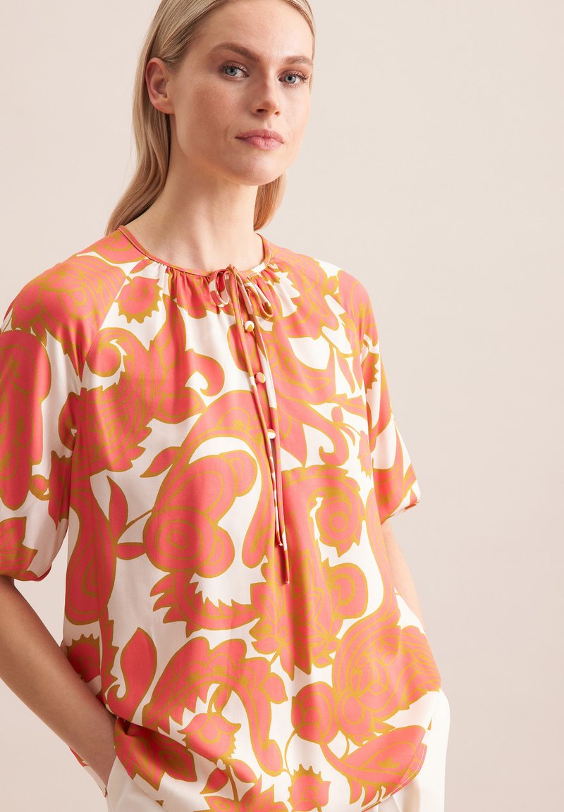 Korte mouwen blouse van lichtgewicht stof met een levendig roze en oranje bloemenpatroon, met een ronde halslijn en knoopsluiting.