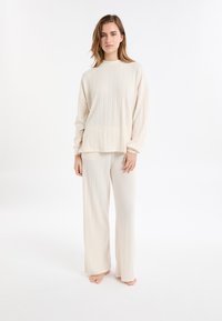 Cremefarbener, gerippter Strickpullover und passende weit geschnittene Hose mit hohem Ausschnitt und lässiger Passform, aus weichem, strukturiertem Stoff gefertigt.