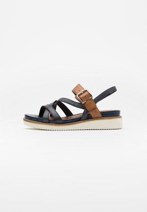 Black and brown leather sandals with cross straps, adjustable ankle strap, and a white platform sole. Textured footbed and buckle detail.
