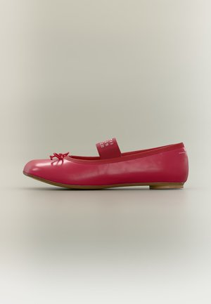 Ballerine plate en cuir rouge avec petit nœud sur le devant et bride élastique sur le dessus, semelle en bois plate, vue de côté sur fond neutre.