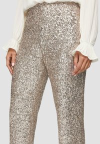 Glanzende, metallic beige paillettenbroek met een slim fit, voorzien van een hoge taille en een zachte textuur, gecombineerd met een geplooide witte blouse.