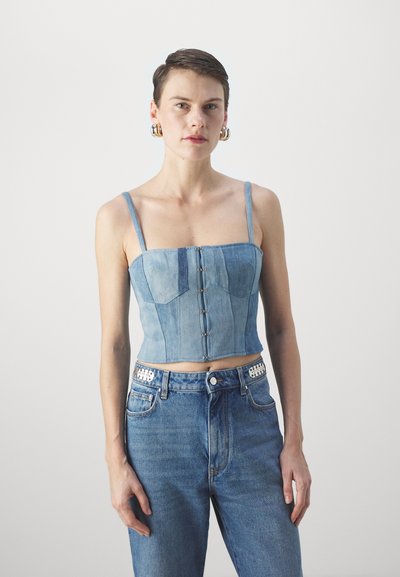 Blå denim crop-top med tynne stropper, frontlukking med knapper, og paneldetaljer. Bært med høy midje blå jeans.