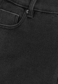 Gros plan sur un jean en denim noir montrant la poche avant, la passants de ceinture et le détail des rivets métalliques.