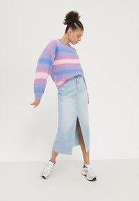 Pull multicolore avec des rayures roses et bleues, associé à une jupe en jean clair avec une fente à l'avant. Porte des baskets argentées de sport.