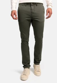 Chinos de ajuste slim en verde oliva, fabricados con una tela suave, que presentan un patrón texturizado sutil y bolsillos estándar. Combinados con zapatillas de color claro.