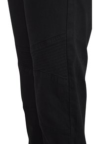 Svarta byxor med en texturerad design och ribbade detaljer vid knäna. Tillverkade av ett slitstarkt tyg med en åtsittande silhuett.