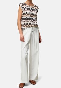 Haut en tricot avec un motif zigzag multicolore, associé à un pantalon en lin blanc ample et des sandales plates marron.