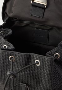 Juodas pintas audinio kuprinės krepšys kibiru, su sidabriniais aklės, užsegimas maža virvele ir lygiu vidiniu pamušalu.