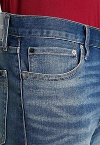 Blå denimjeans med en urtvättad finish, med rak passform, fem fickor och ljusbruna stygn. Metallknapp i midjan.