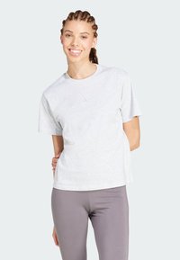 Camiseta gris de manga corta hecha de tela suave. Presenta un cuello redondo y una marca sutil en el frente. Combinada con leggings grises.