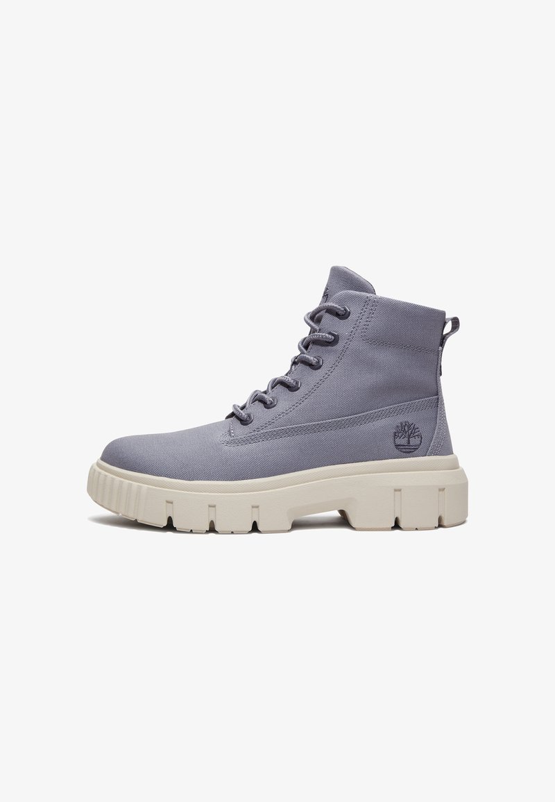 Bottines en toile grises avec une finition texturée, semelle en caoutchouc blanche et six œillets pour les lacets. Présente un logo de marque sur le côté.