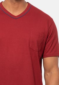 Punainen V-pääntie t-paita, joka on valmistettu pehmeästä puuvillasta. Siinä on rintatasku ja kontrastivärinen sininen reuna kaula-aukossa. Sileä pinta ja rento malli.