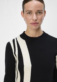 Must mustre, millel on diagonaalsed valged triibud, on valmistatud pehmest materjalist, ümmarguse kaeluse ja soonikute varrukatega.