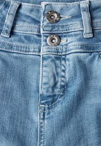 Tela de mezclilla azul clara con textura visible, que presenta dos botones plateados en la cintura, detalles cosidos y un pequeño bolsillo frontal.