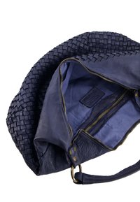 Tmavě modrá kožená kabelka s tkanou texturou, se zipem nahoře a interiérem podšitým jednolitou modrou tkaninou. Disponuje mosaznými kovovými doplňky a má strukturovaný tvar.
