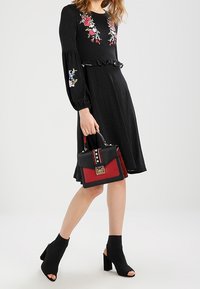Vestido negro con lunares y bordado floral, con volantes. Bolso negro y rojo con tachuelas y herrajes dorados. Botines negros.