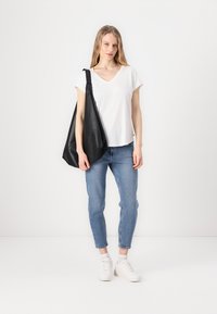 Svart lær totebag over skulderen, hvit V-hals t-skjorte, og lyseblå jeans med avsmalnende passform og oppbrett. Hvite sneakers fullfører antrekket.