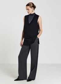 Top senza maniche nero con scollatura a V sovrapposto a un dolcevita grigio; abbinato a pantaloni larghi grigi e scarpe nere lucide.