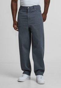 Donkergrijze denimjeans met een relaxte pasvorm, hoge taille en vijf zakken. Afgewerkt met een knoop- en ritssluiting, gecombineerd met witte sneakers.