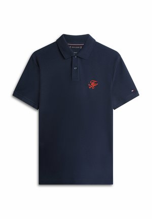 Polo de manga corta azul marino con cuello, dos botones, iniciales bordadas en rojo en el pecho y pequeño logo de bandera en la manga.