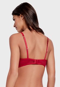 Soutien-gorge rouge avec des bretelles réglables et une fermeture à crochets au dos. Texture lisse, design typique avec un style simple et fonctionnel.