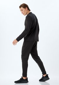 Sort træningsoutfit bestående af en langærmet top og tapered bukser. Stoffet er glat med en mat finish, suppleret med teksturerede accenter og manchetter.