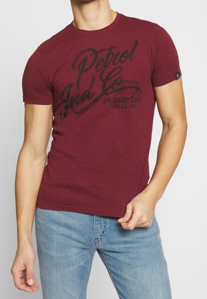 Bordeauxrotes T-Shirt aus Baumwollmischmaterial, mit schwarzem Grafikdruck "Petrol Ind Co" und "Crude Oil 5026.SE" auf der Vorderseite.