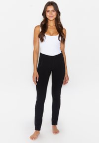 Schwarze, eng anliegende Hosen mit Reißverschlusstaschen, aus einem glatten, elastischen Material, kombiniert mit einem weißen, ärmellosen Top.