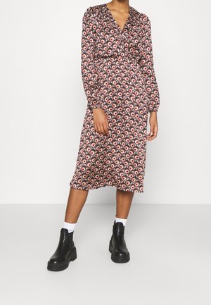 Femme portant une robe midi à manches longues avec un motif floral de marguerites, accompagnée de chaussettes blanches et de bottines noires.