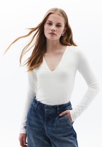 Witte top met lange mouwen en een diepe V-hals, gecombineerd met high-waisted, licht vervaagde blauwe denim jeans. Gladde textuur, eenvoudig ontwerp.