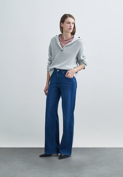 Ανοιχτό γκρι πλεκτό πουλόβερ με κουκούλα, συνδυασμένο με μπλε τζιν παντελόνι φαρδιάς γραμμής. Μαύρα μυτερά παπούτσια συμπληρώνουν το σύνολο. Υφή υφάσματος με casual σχεδιασμό.