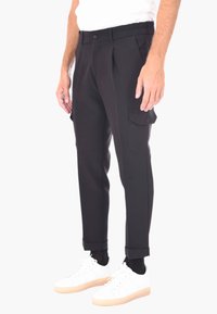 Pantaloni cargo neri a gamba affusolata con tasche laterali e chiusura a bottone, realizzati in un tessuto liscio. I risvolti mostrano delle sneakers bianche.
