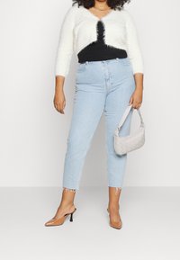 Suéter corto blanco y esponjoso, camiseta negra, jeans de tiro alto en azul claro con dobladillo deshilachado, tacones marrones de punta afilada y bolso trenzado gris.