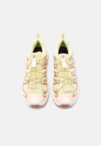 Par teka svetlo rumenih in bež atletskih čevljev z mrežastim materialom, hitro zavezljivimi vezalkami in gumijastimi podplati na belem ozadju.