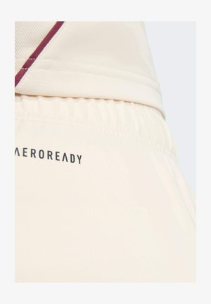 Detail pohledu na béžový elastický pás a část odpovídajícího trička s vínovým pruhem a textem "AEROREADY" na látce.