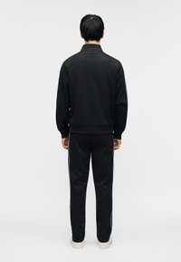 Σετ μαύρου φόρμας με μπουφάν και παντελόνι, με άνετη εφαρμογή, ριμπ μανσέτες και λευκές πλευρικές ρίγες στο παντελόνι. Ομοιόμορφη, λεία υφή σε όλο το σύνολο.