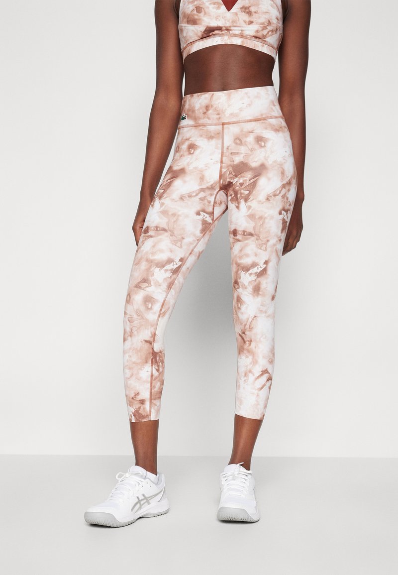 Brun og hvit marmorert sports-bh og capri leggings laget av elastisk stoff; kombinert med hvite treningssko.