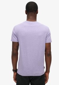 T-shirt in cotone viola con maniche corte, scollatura rotonda e una texture melangiata. Presenta un'etichetta del marchio discreta sul lato sinistro.