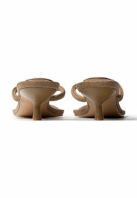 Paire de sandales à talons kitten en daim beige, vues de dos sur une surface blanche avec les détails des brides visibles.