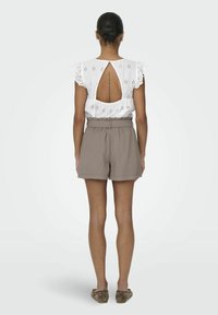 Witte top met korte mouwen en een oogjesdesign, met een sleutelgat achterkant, gecombineerd met bruine high-waisted shorts met een relaxte pasvorm en een elastische tailleband.