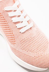 Růžové síťované tenisky s texturovaným svrškem, bílými šňůrkami a hladkou bílou podrážkou, zdůrazňující prodyšný materiál a moderní design.