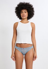 Camiseta sin mangas blanca de algodón con un ajuste relajado, combinada con bragas de encaje azul claro con borde festoneado y un pequeño detalle rosa en el centro.