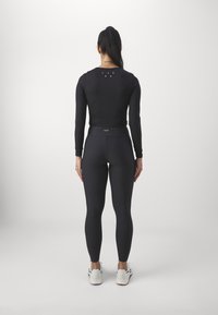 Black long-sleeve top with a round neck and printed logo on the back, paired with form-fitting black leggings and white athletic shoes.