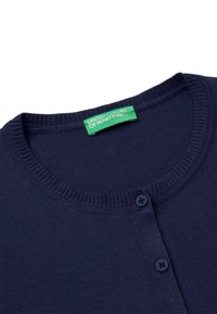Námořnický modrý kardigan s kulatým výstřihem, vroubkovanými okraji a dvěma tmavými knoflíky. Štítek nese nápis "United Colors of Benetton."