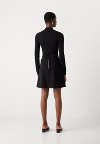 Haut à manches longues noir associé à une jupe évasée noire. La jupe possède une fermeture éclair au dos et une texture lisse. Design uni sur l'ensemble.