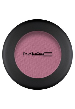 Rund blush-kompakt med en matt svart overflate. Inneholder et mykt rosa pudder, med en strukturert overflate og et merkevarsle.