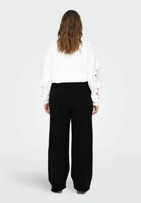 Sweatshirt blanc avec des découpes florales sur les manches, associé à un jean noir à taille haute et coupe large. Design minimaliste et décontracté.